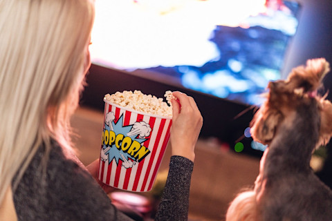 Woman eating popcorn while watching TV with dog