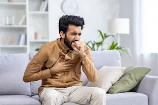 Young man on the couch coughing and suffering from bronchitis