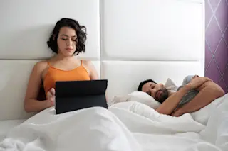 awake asleep couple bed laptop - Shutterstock