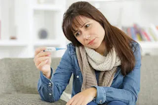 Woman taking her temperature, fever - Shutterstock