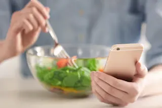 Woman eating a salad and logging meal calories Noom app concept - shutterstock
