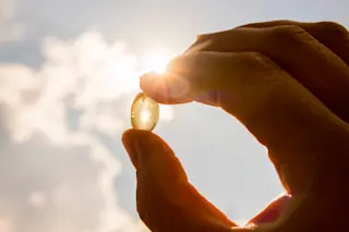 hand holding a vitamin d pill against the sunlight sky - shutterstock 1148454926