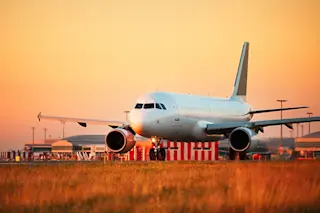 airplane is grounded against a sunset orange yellow sky - shutterstock