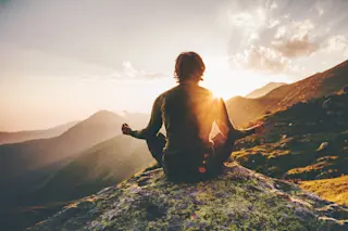 person is meditating on a mountain - shutterstock 617840372