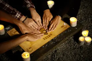 Three people conducting a seance using a Ouija Board with white candles. Shot from overhead.
