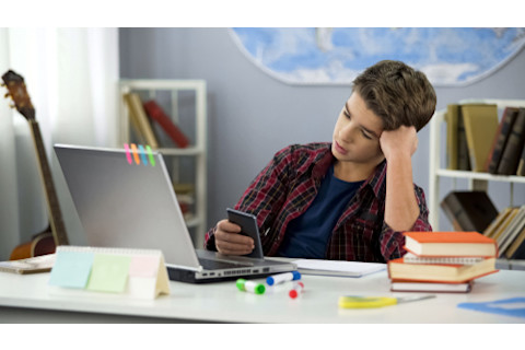 teen scrollling on phone instead of doing homework