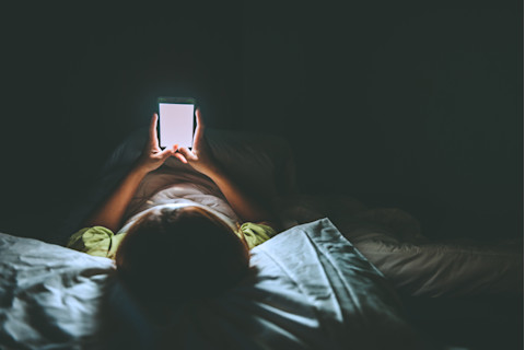 Smartphone addiction, person laying in bed with phone at night