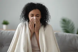 Woman blowing her nose showing a common cold symptom of HMPV 