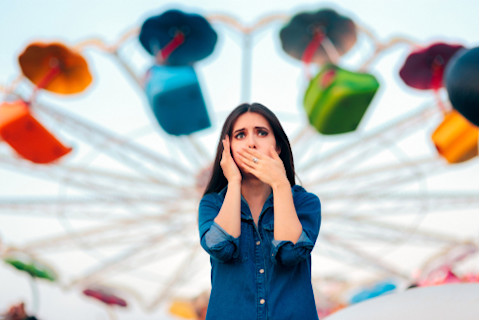 dark-haired-woman-covers-mouth-near-roller-coaster