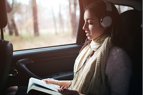 woman-in-back-seat-of-car-with-green-scarf-and-large-headphones-reading-a-book