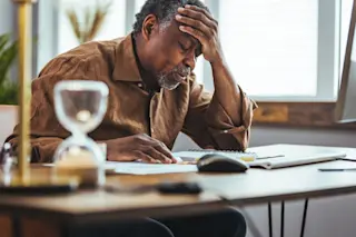 older man stressed reading book. hour glass in foreground