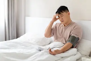 man laying in bed checking with high blood pressure caused by stress
