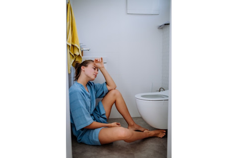 young woman sitting on floor of bathroom by toilet with stomach flu