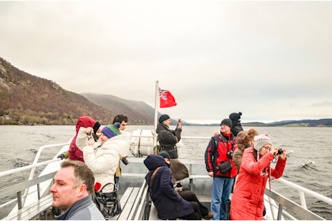 Loch Ness, Scotland/United Kingdom -Jan 2nd 2013: International tourists taking pictures on tour cruise on the famous Loch Ness in the Scottish Highlands on a cloudy winter day.