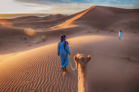 Two Tuareg nomads leading a camel in the Sahara Desert, Morocco.