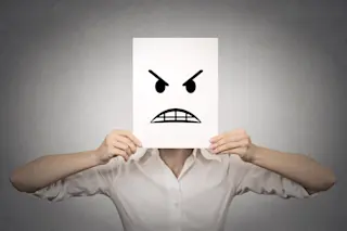 woman holding an angry face drawn on paper in front of her face