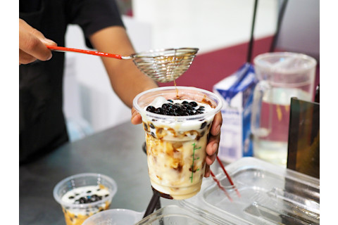 Pouring brown sugar pearl (boba) over glass of iced fresh milk