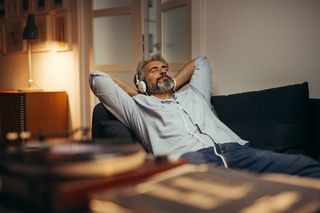 Man reclining on his couch listening to vinyl records through headphones 
