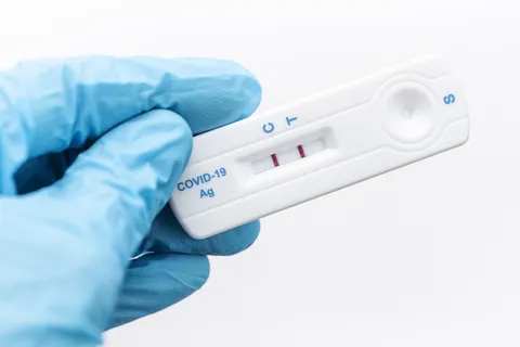 gloved hand holding positive COVID-19 test