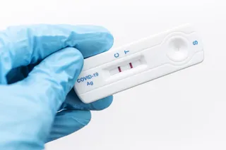 gloved hand holding positive COVID-19 test