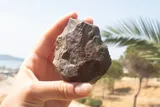 A hand holds a handaxe against an idyllic background.