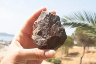 A hand holds a handaxe against an idyllic background.