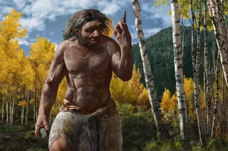 An ancient human stands in a forest, holding a stone and a stone point. 