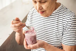 an older woman eating pink yogurt