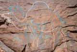 Carvings of animals, outlined in white and blue, overlaid on top of a panel of rock, including three camels and three gazelles.