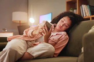 a young woman sits on her couch scrolling on her phone a young woman sits on her couch scrolling on her phone