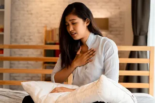 woman sitting on a bed struggling to breathe 