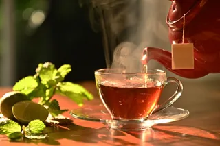 black tea in a clear glass tea cup while hot tea is poured from brown clay teapot