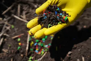 yellow gloved hand holding soil with plastic pieces in it 