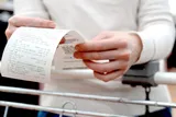 person holding a shopping receipt while leading on a shopping cart 