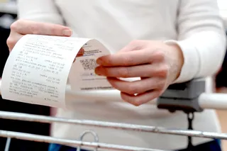 person holding a shopping receipt while leading on a shopping cart 