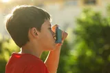 child in a red t-shirt using an inhaler 