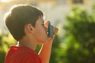 child in a red t-shirt using an inhaler 