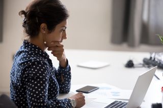 Woman sitting at her desk with a computer, contemplating a decision