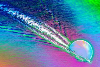 a multi-colored illustration of a quark zooming through plasma and creating ripples 