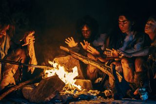 group of early humans dressed in furs sitting around a fire