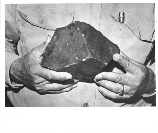 a black and white photo of a close up of a man holding a black meteorite