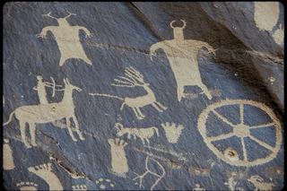 Black stone wall with white petroglyphs carved into it. 