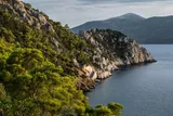 Rocky coastline of Greece’s Methana volcano with forested cliffs and sea, shaped by past volcanic magma activity