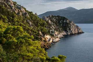 Rocky coastline of Greece’s Methana volcano with forested cliffs and sea, shaped by past volcanic magma activity