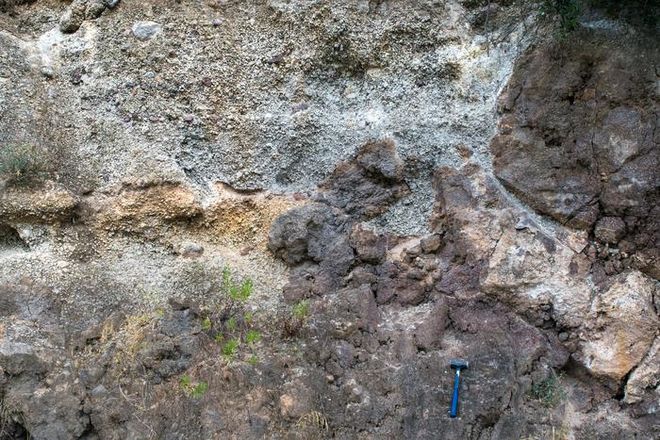 Red lava and white pumice deposits from a prehistoric eruption of Methana volcano in Greece, visible in exposed rock layers