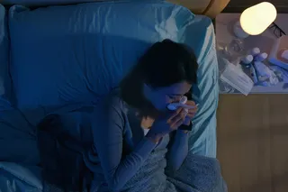 Person with a cold lying in bed at night, blowing their nose, illustrating how the immune system can make symptoms feel worse after dark.