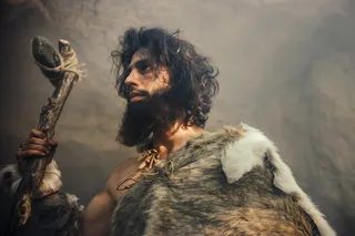 early human, dressed in furs, holding a stone tool 