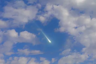 A meteorite streaking through a blue and cloudy sky