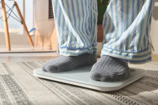 Person standing on a bathroom scale, representing BMI, body weight, and obesity health risk measurements.
