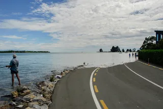 A road flooded by the sea, while a person fishes off to the side 